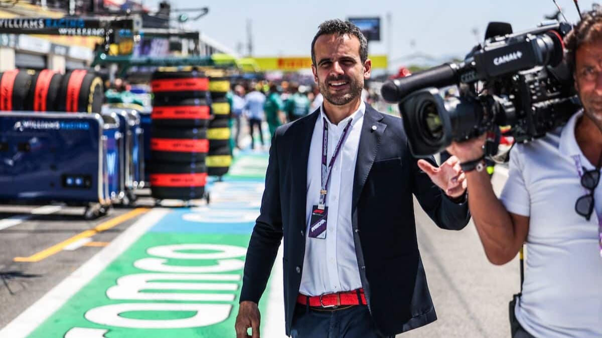 Laurent Dupin, présentateur Canal+, sourit en marchant dans la voie des stands d'un Grand Prix de F1, filmé par un caméraman de la chaîne.