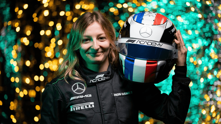 Doriane Pin souriante tenant son casque de pilote Mercedes avec des lumières colorées en arrière-plan