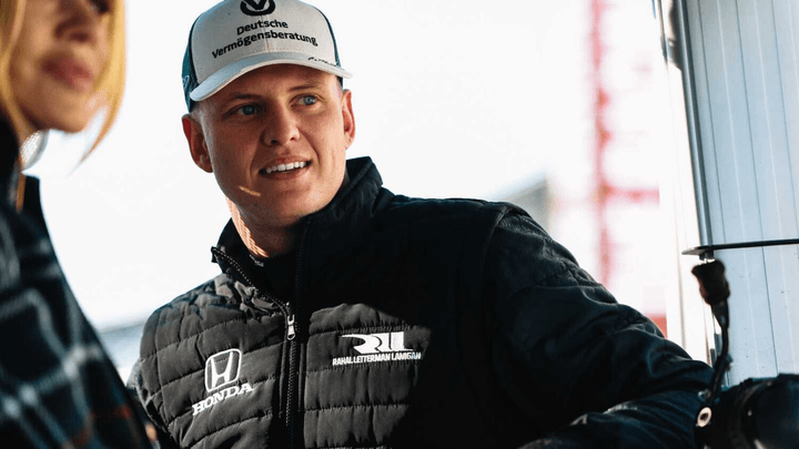 Mick Schumacher souriant en combinaison de pilote dans le paddock