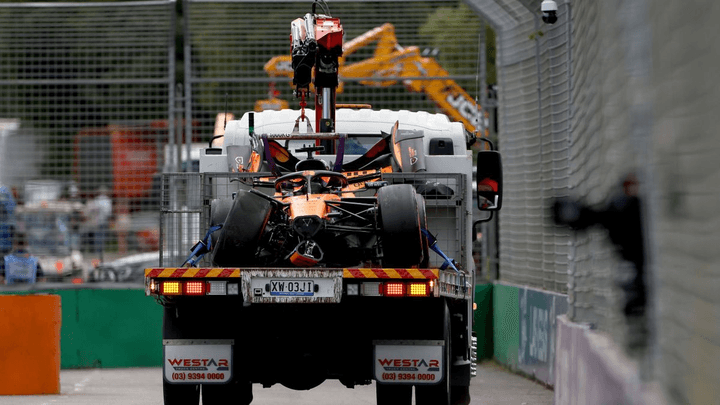 Voiture de F1 McLaren orange immobilisée sur le circuit avec des mécaniciens intervenant