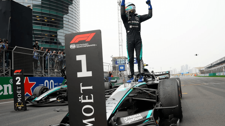 Pilote de Formule 1 célébrant sa victoire debout sur sa monoplace, bras levés en signe de triomphe sur le circuit de Shanghai