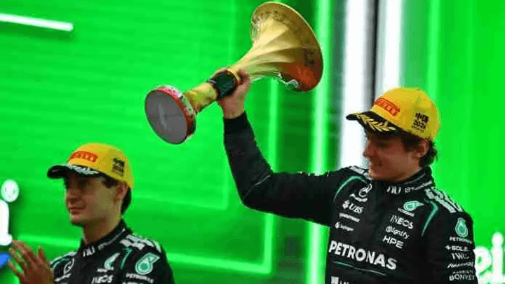 Pilote de F1 Mercedes brandissant un trophée doré sur un podium avec fond vert Heineken