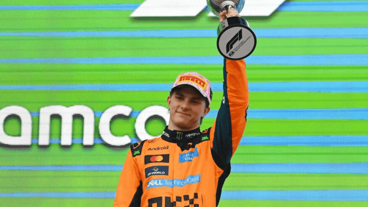 Pilote en combinaison orange McLaren brandissant un trophée sur le podium F1