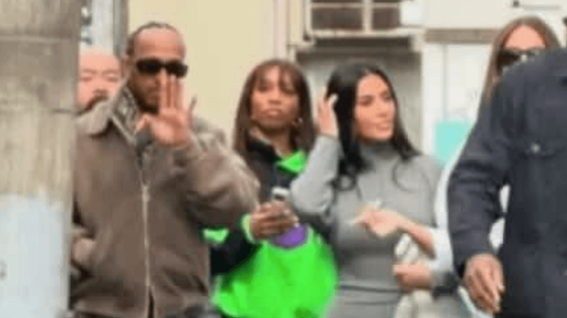 Lewis Hamilton fait un geste de la main lors d'un déplacement, accompagné de plusieurs personnes