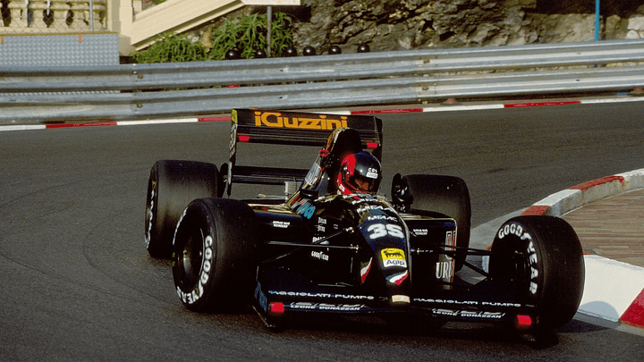 Voiture Andrea Moda Formula de 1992 en action sur circuit avec pilote au volant