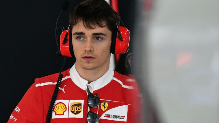 Charles Leclerc en combinaison Ferrari rouge avec casque audio dans le paddock F1