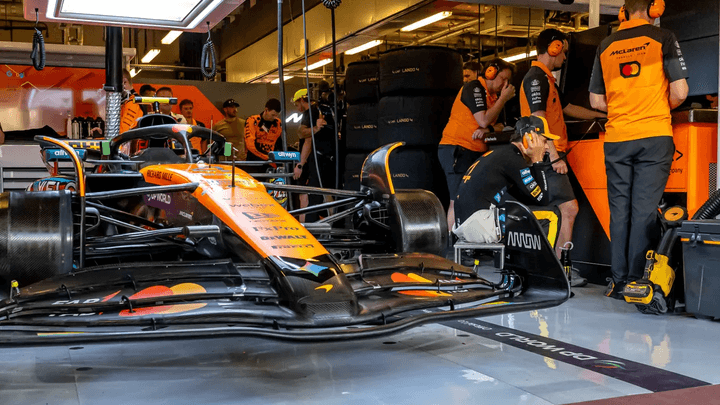 Monoplace McLaren orange dans le garage avec mécaniciens en combinaison orange