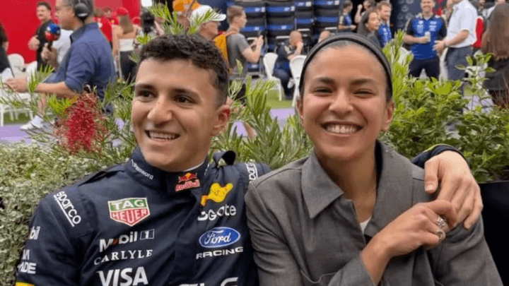 Pilote Red Bull Racing en combinaison Oracle avec une femme souriante dans le paddock F1