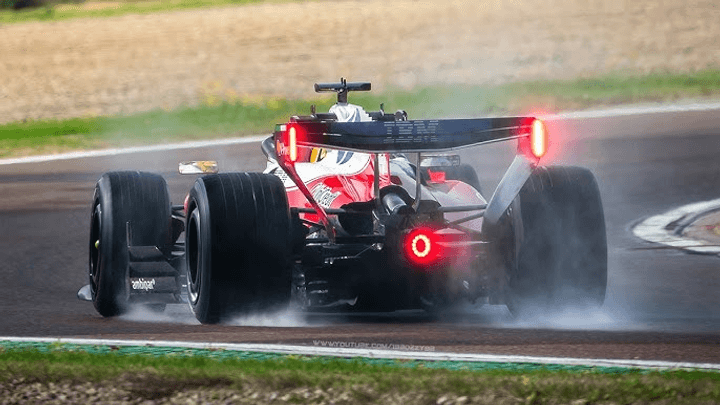 Ferrari F1 rouge roulant sous la pluie avec spray d'eau visible