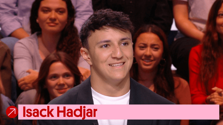 Isack Hadjar souriant lors d'une interview télévisée, assis dans un plateau TV avec du public en arrière-plan