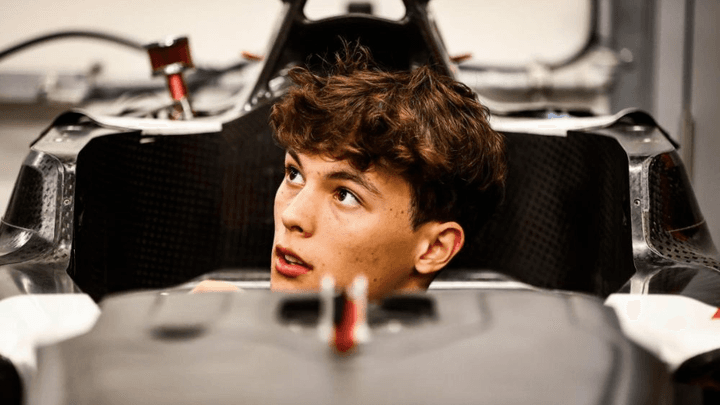 Jeune pilote de F1 assis dans son cockpit, regardant vers la droite dans le garage