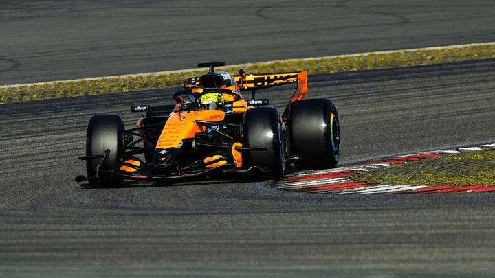 Monoplace McLaren orange en action sur circuit, virage serré avec bordures rouges et blanches