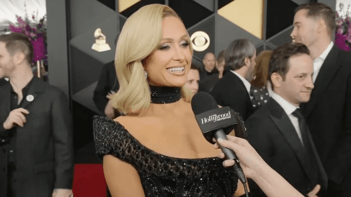Femme blonde en robe noire pailletée interviewée sur tapis rouge lors d'un événement officiel