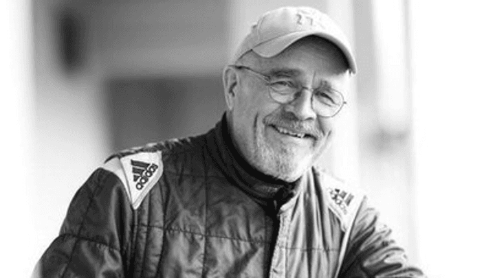 Portrait en noir et blanc d'un homme âgé souriant, portant casquette et veste de course