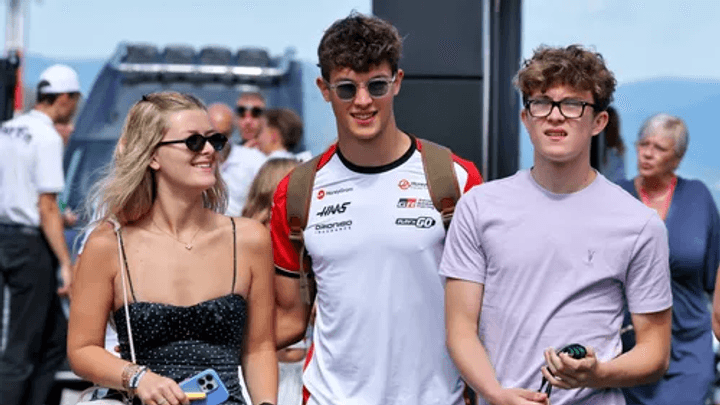 Pilote F1 en polo Haas posant avec deux jeunes fans lors d'un événement paddock