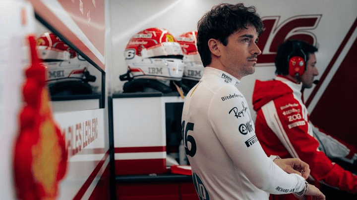 Pilote Ferrari en combinaison blanche dans le garage avec casques et équipement F1 visible