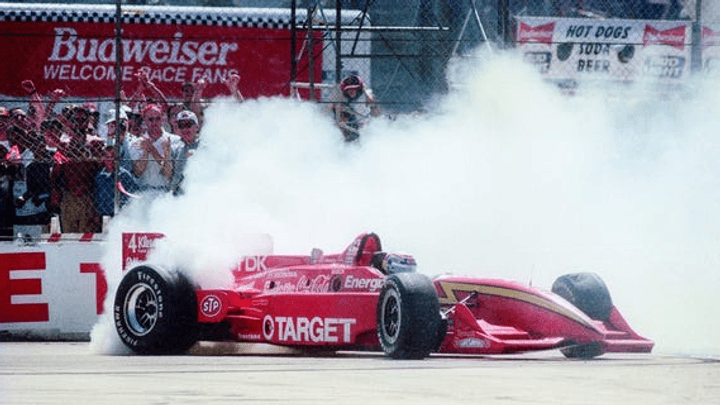 Alex Zanardi en action au volant de sa monoplace rouge Target en IndyCar, déployant un nuage de fumée sur la piste