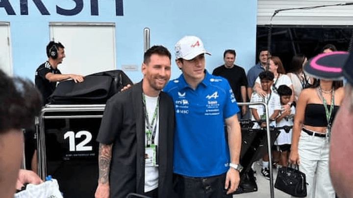 Pilote Alpine F1 en polo bleu posant avec un fan tatoué devant une voiture F1 noire