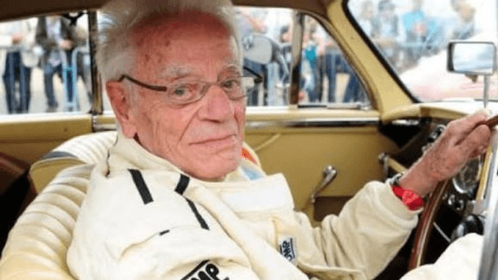 Homme âgé avec lunettes au volant d'une voiture vintage beige, portant une veste claire