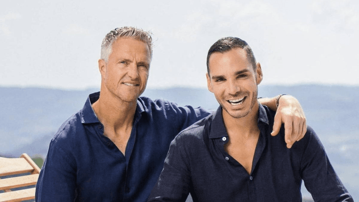 Deux hommes en chemises bleues posent ensemble devant un paysage maritime