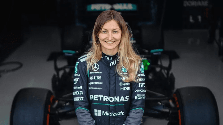 Pilote féminine souriante en combinaison Mercedes-AMG Petronas devant monoplace F1 turquoise