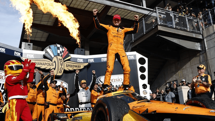Pilote célébrant sa victoire sur sa monoplace orange à Indianapolis avec feux d'artifice