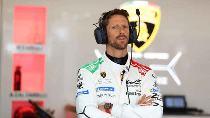 Romain Grosjean en combinaison de course blanche avec casque, bras croisés dans le paddock F1
