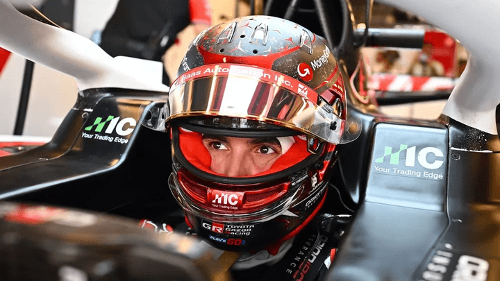 Pilote F1 dans son cockpit avec casque rouge et noir, sponsors MIC visibles sur la monoplace