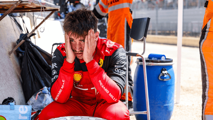 Charles Leclerc assis dans son garage Ferrari, la tête dans les mains en signe de déception