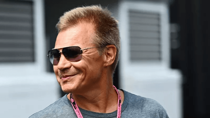 Homme avec lunettes de soleil et badge F1 rose souriant dans le paddock
