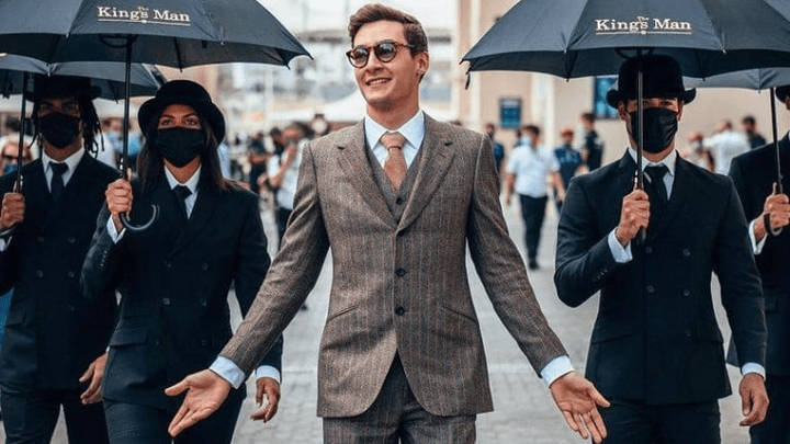 Homme en costume marchant entouré de gardes du corps avec parapluies dans une rue